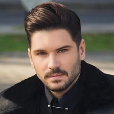 a close up of a person wearing a black shirt and jacket with a beard, looking at the camera