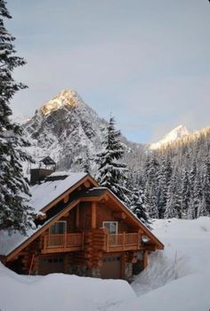 a log cabin in the snow with mountains in the back ground and trees on either side