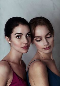 two beautiful women standing next to each other in front of a white wall with their eyes closed