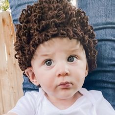 a young child with curly hair sitting on someone's lap looking at the camera