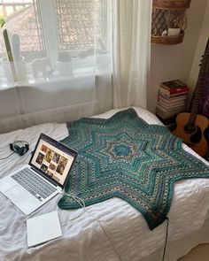 an open laptop computer sitting on top of a bed next to a blanket and guitar