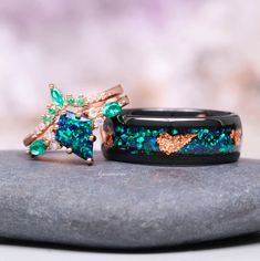 two rings sitting on top of a rock with green and pink stones in the middle