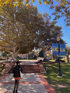 a woman is walking down the sidewalk in front of a sign that says ucla