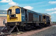 a yellow and black train is on the tracks next to a building with a sky in the background