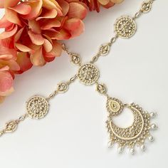 a close up of a necklace on a white surface with flowers in the foreground