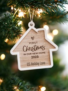 a wooden ornament hanging from a christmas tree with lights in the background and a first christmas in our new home sign