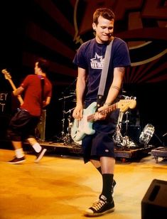 two young men playing guitars on stage with one man in the foreground and another standing behind them