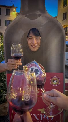 two people toasting wine glasses in front of a large bottle and glass holder with an image of a woman on it