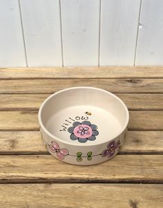 a bowl with flowers painted on it sitting on a wooden table next to a wall