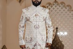 a man standing in front of a wall wearing a white outfit with intricate designs on it