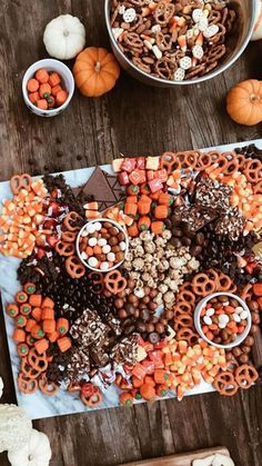 a wooden table topped with lots of candy and candies next to bowls of pumpkins