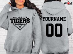 Personalized Tiger School Spirit T-Shirt Crewneck, Hoodie Hooded Sweatshirt Football, Baseball, Basketball, Softball, Track, Volleyball, Cross Country, Cheer, Wrestling Not all colors are available in all sizes and styles.  Please check the color and size charts in photos. We do our best to accurately represent shirt colors by using actual photos but do understand that all monitors will display differently. Please contact us prior to purchase with any questions on sizing or colors. Your purchase Gray Letter Print Hoodie For Sports Events, Baseball Season Crew Neck Sweatshirt With School Spirit, Athletic Heather Hoodie With Letter Print For Sports, College Team Name Hoodie Tops, Baseball Season Team Spirit Cotton Sweatshirt, School Spirit Graphic Sweatshirt For Baseball Season, Gray Crew Neck Hoodie For Sports Events, College Team Name Hoodie, Sporty Pre-shrunk Hooded Tops