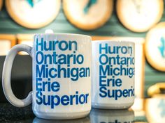 two coffee mugs sitting on top of a counter next to each other in front of clocks