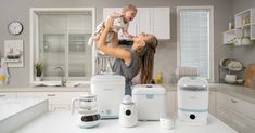 a woman holding a baby up in the air while standing next to appliances and blenders