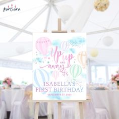 an easel with a sign that says welcome to the first birthday on it and balloons in the background