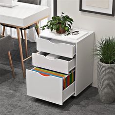 a white desk with three drawers and a potted plant on the table next to it