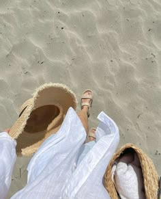 a person laying on top of a sandy beach next to a straw hat and flip flops