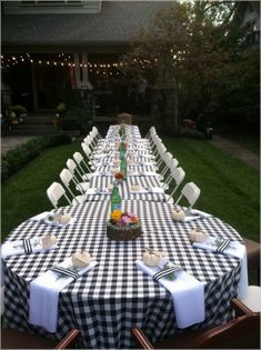 a long table with black and white checkered cloths is set up in front of a house