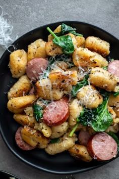 a black plate topped with pasta and sausage