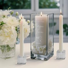 three candles are sitting on a table next to a vase with white flowers and greenery