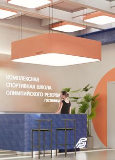 a woman standing behind a blue counter in an office lobby with orange and white accents