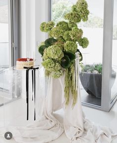 a vase filled with green flowers sitting on top of a white floor next to a cake