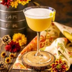 a glass filled with yellow liquid sitting on top of a wooden table next to flowers