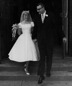 a bride and groom walking down the steps together in black and white, holding hands