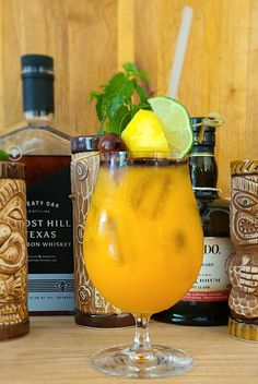 a glass filled with orange juice and garnish next to bottles of alcohol on a wooden table