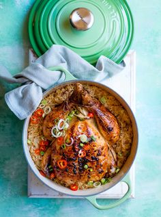 a chicken and rice dish in a pot with a green lid on a blue table