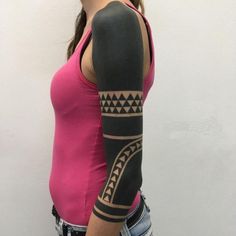 a woman with a pink shirt and black arm sleeve tattoo on her left arm is standing in front of a white wall