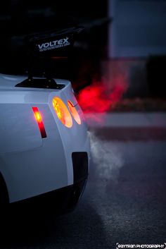 the back end of a white sports car with fog coming from it's exhaust