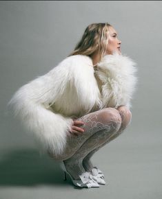 a woman in white fur coat sitting on the ground with her legs crossed and hands behind her back