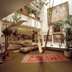 a living room filled with lots of plants and hanging items on the wall next to couches