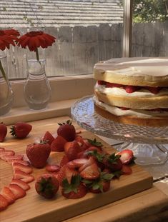 strawberry shortcakes and strawberries on a wooden cutting board next to a window