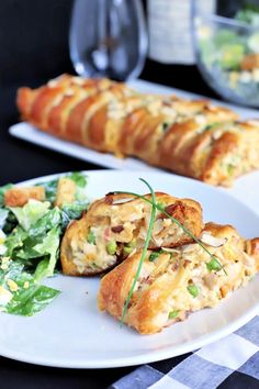 two white plates topped with pastries next to a salad and bread roll on a table