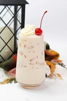 a glass filled with whipped cream and topped with a cherries garnish next to a lantern