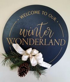 a welcome sign hanging on the side of a wall with a pine cone and bow