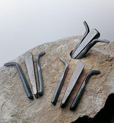 several metal tools are laying on top of a large piece of rock with nails sticking out of it