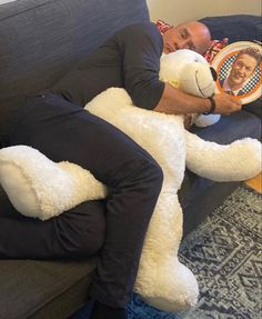 a man laying on top of a couch holding a large white teddy bear in his arms