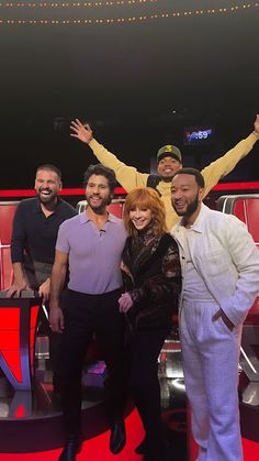 three men and one woman standing in front of a red chair with their arms up