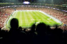 a large stadium filled with people watching a soccer game on the television screen at night