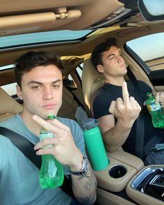 two young men sitting in the back seat of a car holding bottles and pointing at something