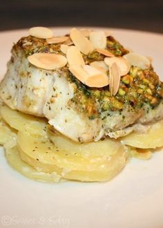 a white plate topped with fish and potatoes covered in pesto, almonds on top