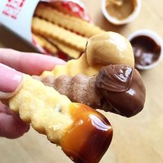 a person holding up a piece of food in front of some dipping sauces and crackers