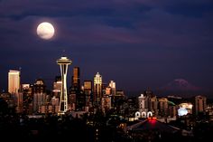 the full moon rises over seattle skyline at night