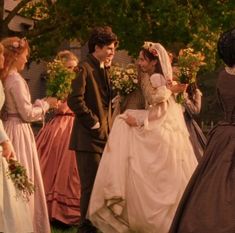 a group of people standing around each other wearing dresses and holding flowers in their hands