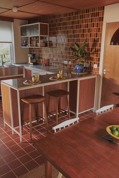 a kitchen with two stools in front of the counter and an island that has fruit on it