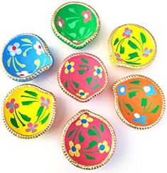 six painted eggs sitting in a circle on a white surface with green leaves and flowers