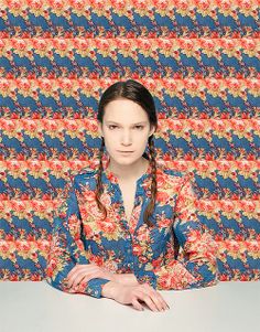 a woman sitting at a table in front of a colorful wall with an intricate pattern